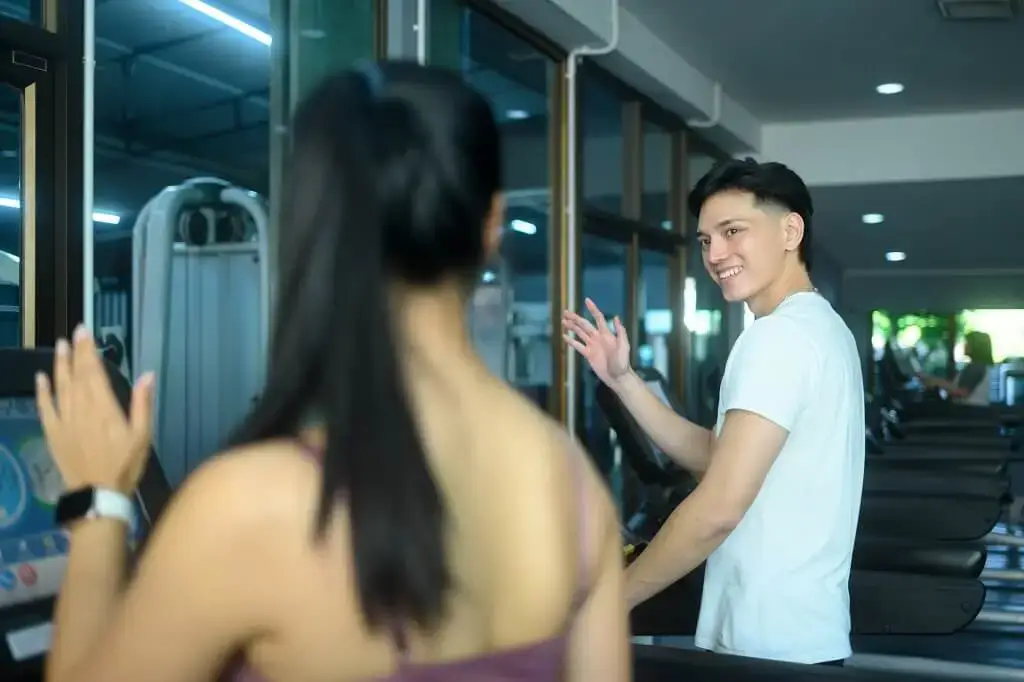A personal trainer waving to his client in the gym