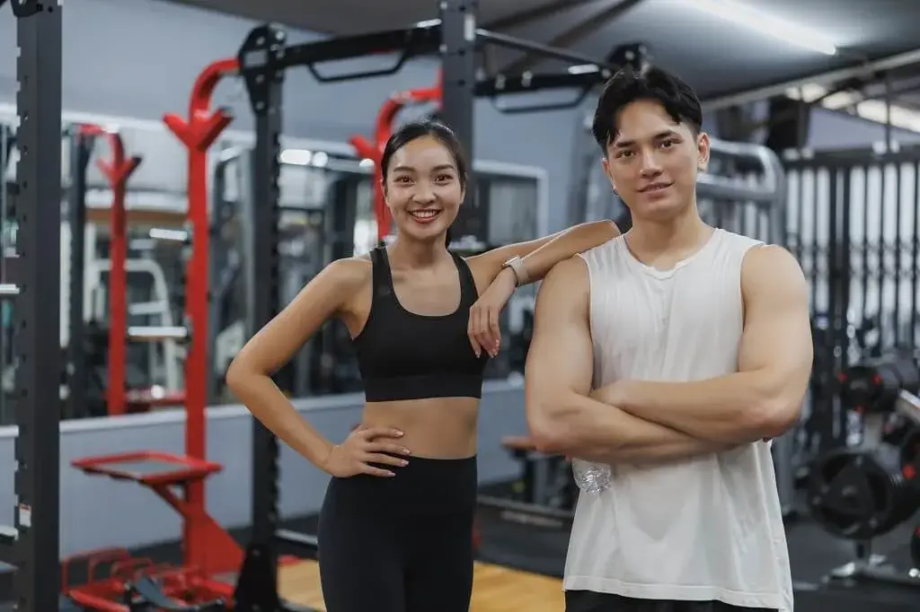 Man and woman smiling in a gym with a personal trainer in Sengkang and Punggol.