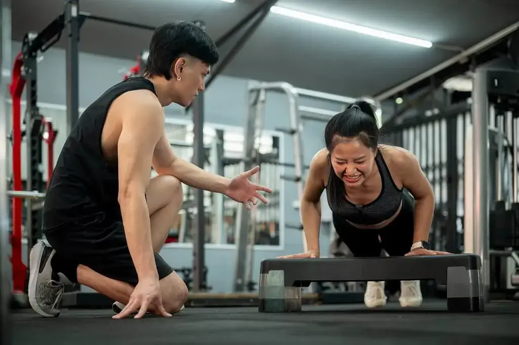 Woman doing push-ups with a personal trainer at a gym in Punggol, Singapore.
