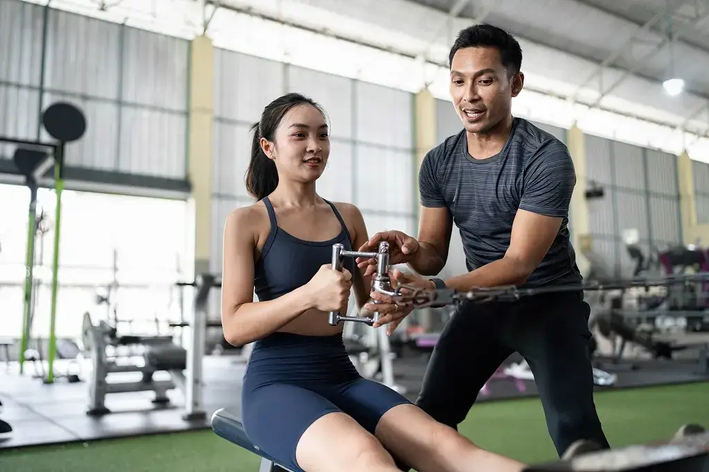 Woman training on a rowing machine with a certified personal trainer in Singapore.